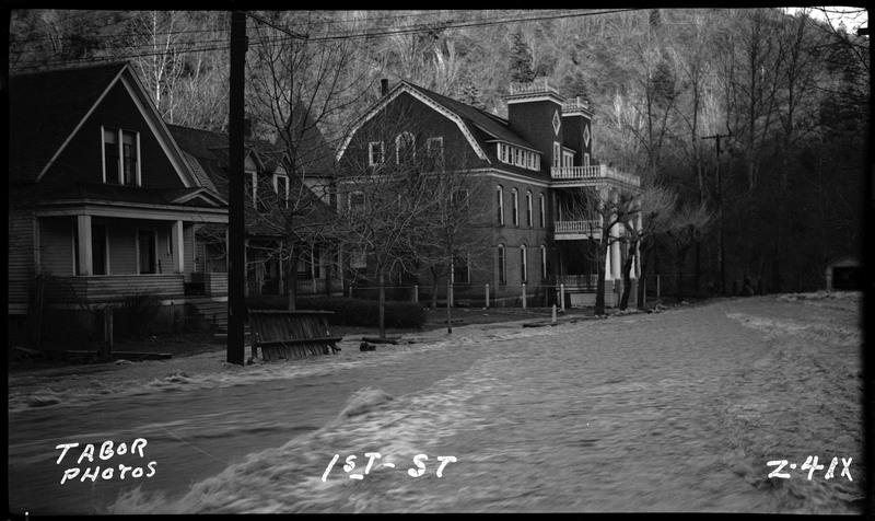 1st Street in Wallace, Idaho during a flood. There is water overflowing in the streets and up to the houses.