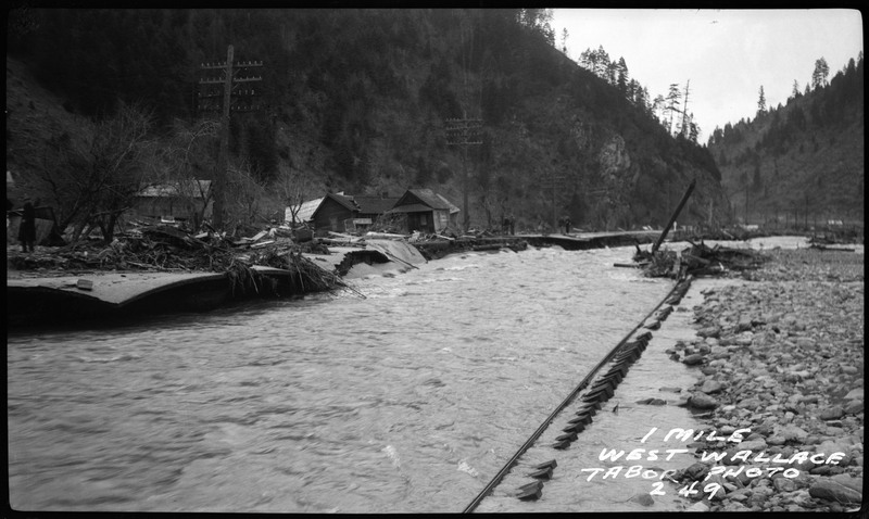 1 mile west of Wallace, Idaho during a flood. There are several damaged buildings in the background.