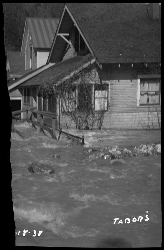Flooding in Wallace, Idaho. Water is flowing onto a porch of a house. The photo is damaged along the left edge.