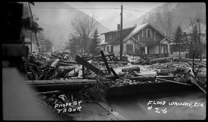 Debris fill the streets during the Placer Creek flood. An unidentified man can be seen standing among the piles of debris.