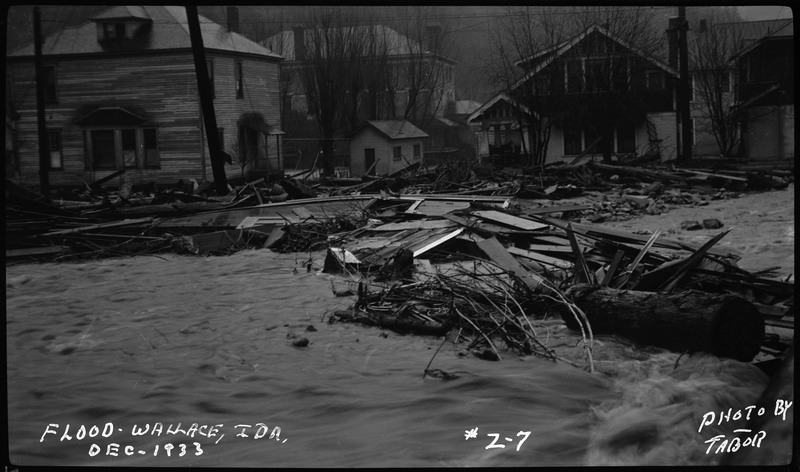 Street view of a flood in Wallace, Idaho with debris and water filling the streets.