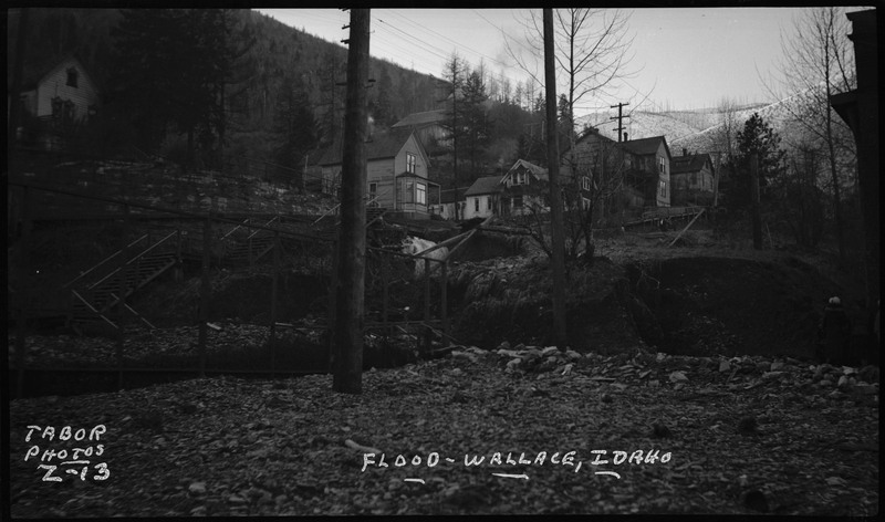 Aftermath of flood in Wallace, Idaho. Image taken looking up from the side of a hill onto houses, possibly depicting mudslides caused by flooding.