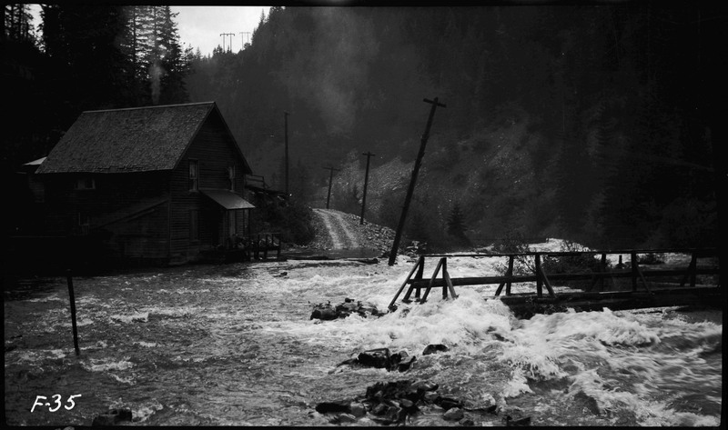 Flood waters rushing over bridge during Placer Creek flood. A building is on the left.