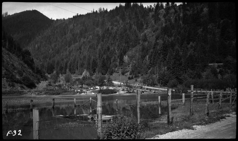Landscape image in Wallace, Idaho. A fence borders a body of water with a road in the distance. 