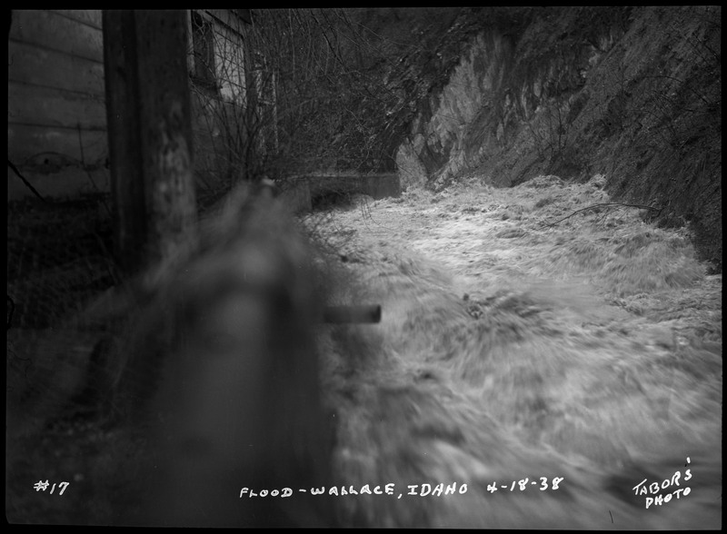 View of rushing water flowing near a building and hillside.