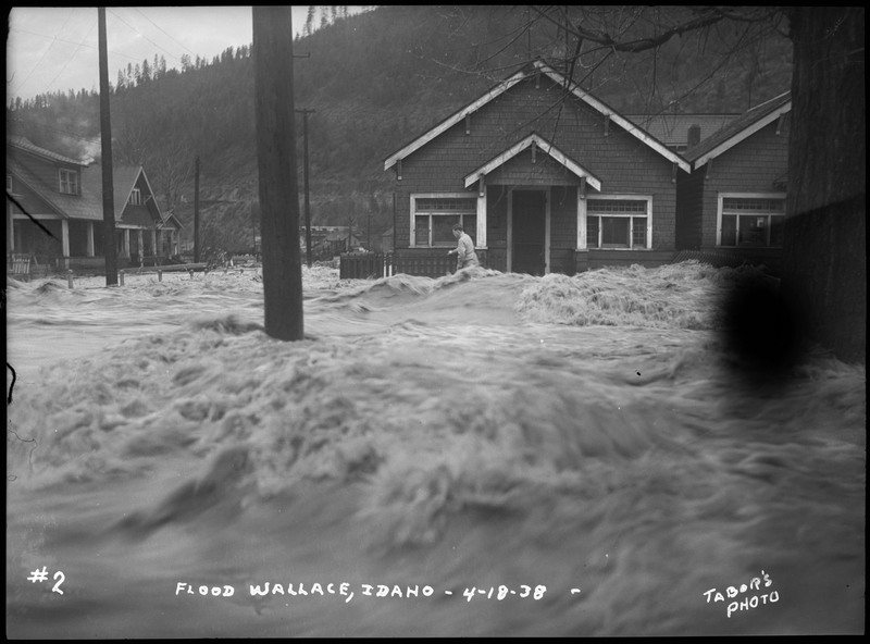 A person wades through the floodwaters in a neighborhood during the Wallace flood. Several telephone poles are in the background.