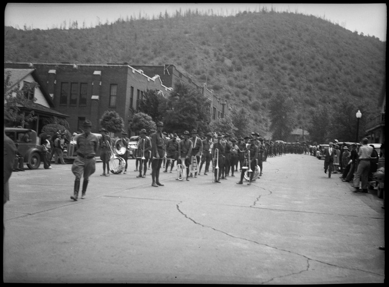 The marching band members holding instruments during the Miner Picnic parade as people watch on the sides of the streets.