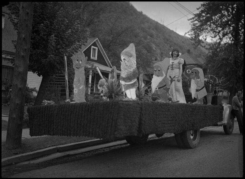 A woman dressed up as Snow White and cut outs of the Seven Dwarves on a parade float. A man is leaning on the side of the car on the left.