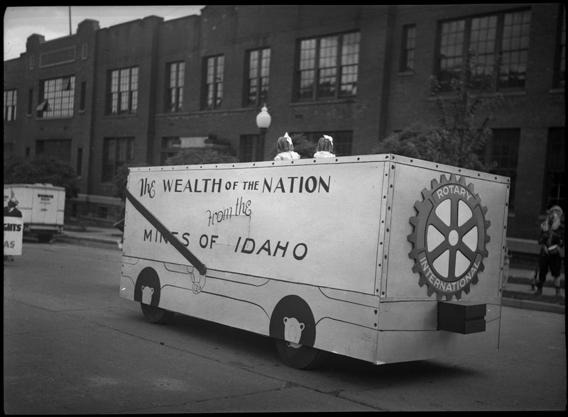 Two young girls sitting on the Rotary club parade float. Text of the float reads, "The Wealth of the Nation from the Mines of Idaho." There is a cut out of the Rotary club logo is on the side. 