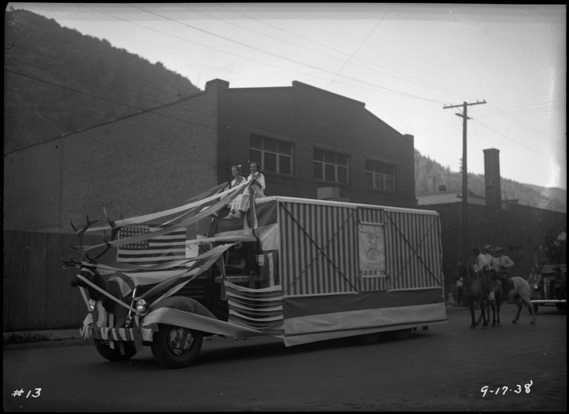 Two girls on the Elks float during the Benevolent Protective Order of Elks Roundup parade. They are pulling on an elk's head that is fixed to the front of the vehicle.