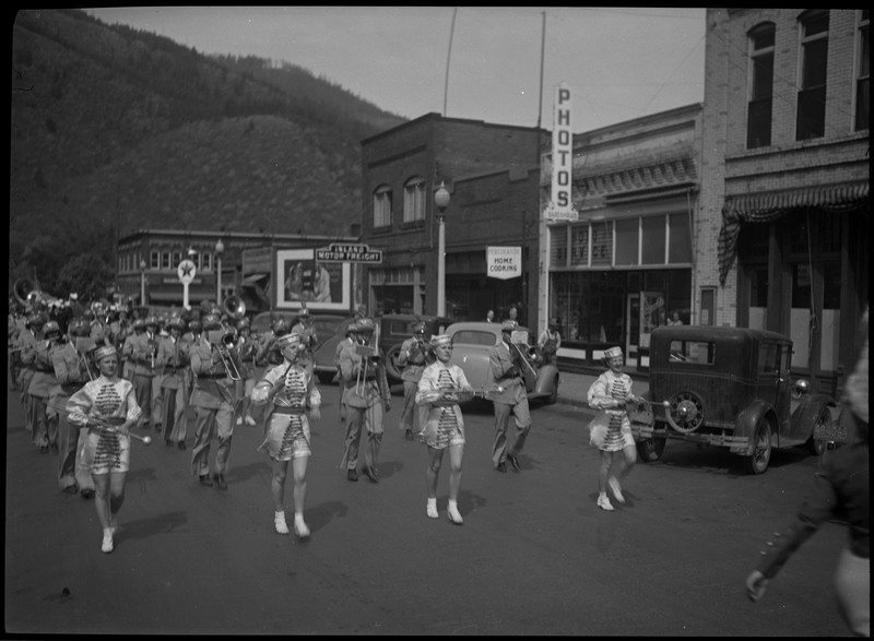 Band members, a few women and mostly men, in the Benevolent and Protective Order of Elks parade. Spectators are watching near the cars parked on the street.