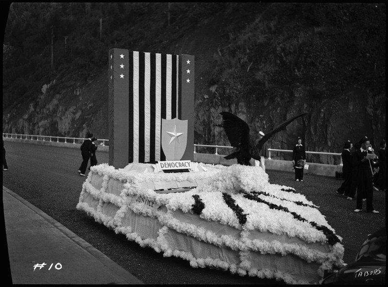 Parade float decorated with stars, stripes, and an eagle with a sign reading, "Democracy." 
