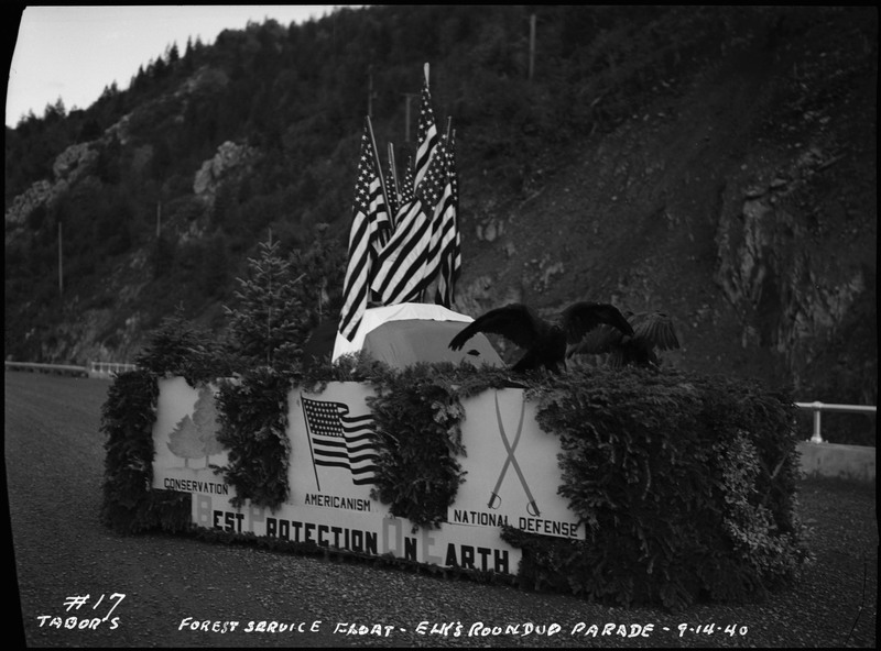 The Forest Service float in the Benevolent and Protective Order of Elks parade. The float is decorated with American flags, eagles, foliage, and signs that read, "Conservation, "Americanism," and "National Defense."