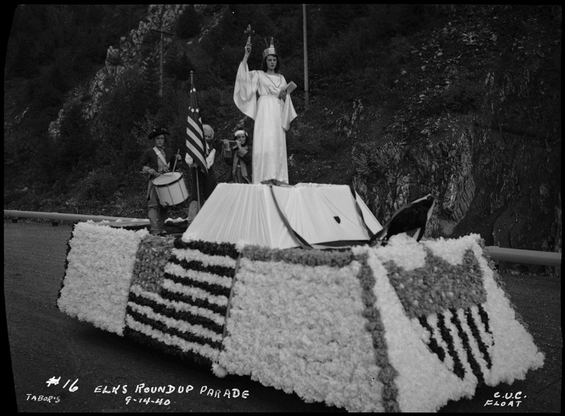 A woman posing like the Statue of Liberty and three people in colonial style clothing on the C.U.C. float during the Benevolent and Protective Order of Elks parade.