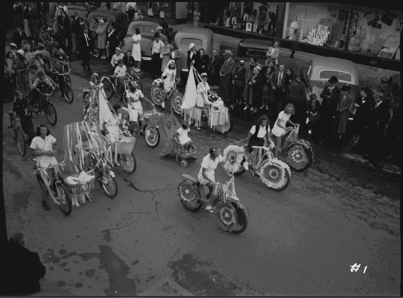 Children on decorated bikes during the Benevolent and Protective Order of Elks parade. Spectators watch from the sidewalk and by parked automobiles.