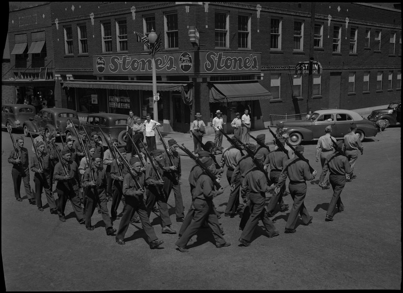 Co. K. Kellogg home guards rounding a corner during a July 4th parade. They are wearing uniforms and holding rifles on their shoulders.
