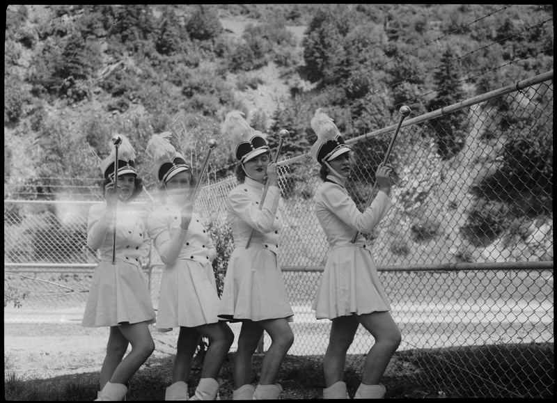 Drum majorettes posing and holding their batons during July 4th parade. They wear identical outfits and shoes.