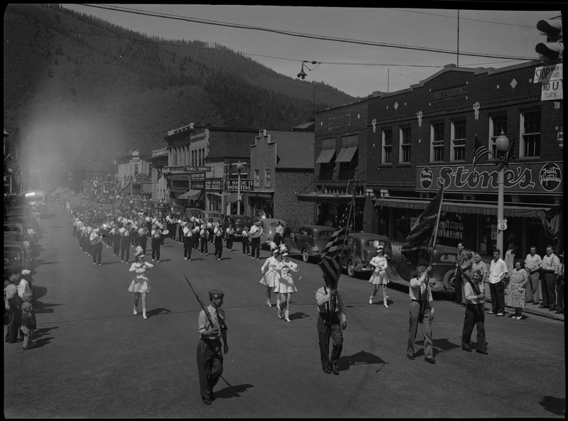 Marching band and majorettes in July 4th parade. Spectators watch the parade procession from the sides of the street.