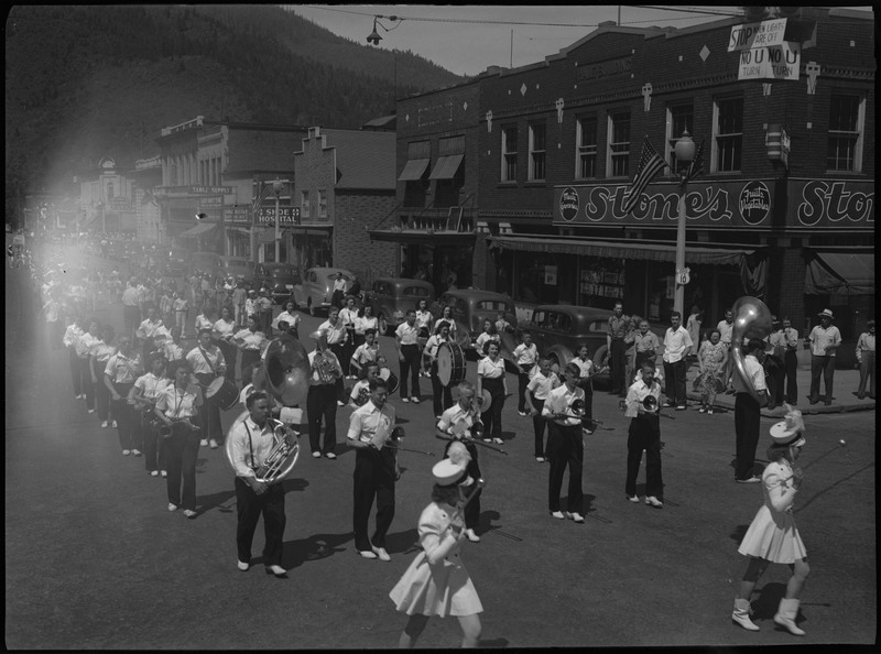 Marching band and majorettes in July 4th parade. Spectators watch the parade procession from the sides of the street.