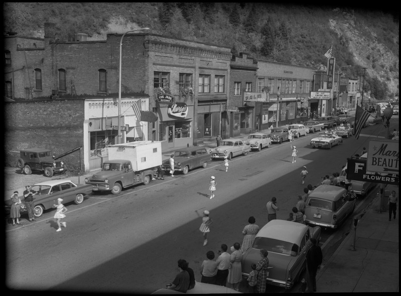 Children in Benevolent and Protective Order of Elks roundup parade. Spectators watch by parked cars along the side of the street.