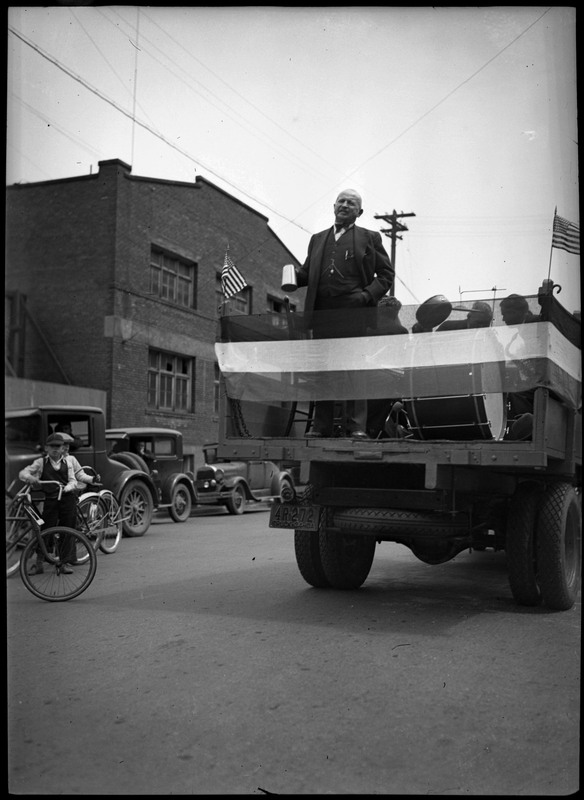 Man standing in the back of a truck during Sunset Brewery parade. Two boys stand with their bicycles on the left.
