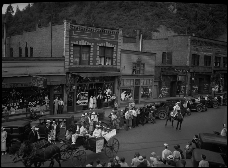 Horse-drawn carriage in the street during the Benevolent and Protective Order of Elks parade. Spectators watch from the sides of the street near parked cars.