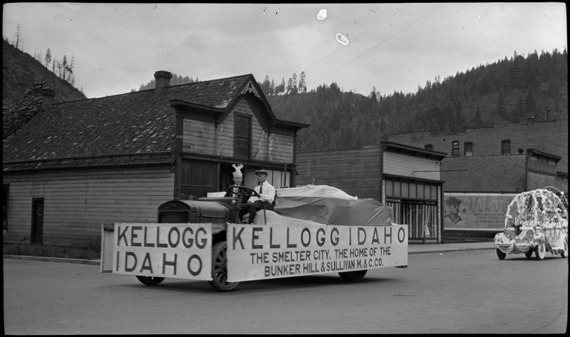 Two people sitting in a Kellogg, Idaho float during the Benevolent and Protective Order of Elks parade. The side of the float vehicle reads, "Kellogg Idaho The Smelter City, The Home of the Bunker Hill & Sullivan M. & C. Co."