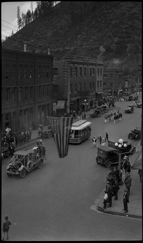 Overhead view of floats and people walking down the street during the Benevolent and Protective Order of Elks parade. An American flag hangs over the street. Spectators watch from the sidewalk.