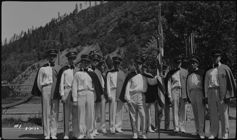 Men wearing matching white uniforms, capes, and hats pose during the Memorial Day parade.