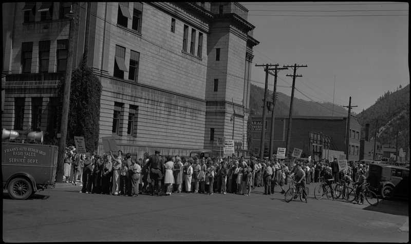 Many children gather in the street for a back-to-school parade. Some are holding signs. A Frank's Auto Repair Shop Radio Sales & Service Dept. truck can be seen on the left.