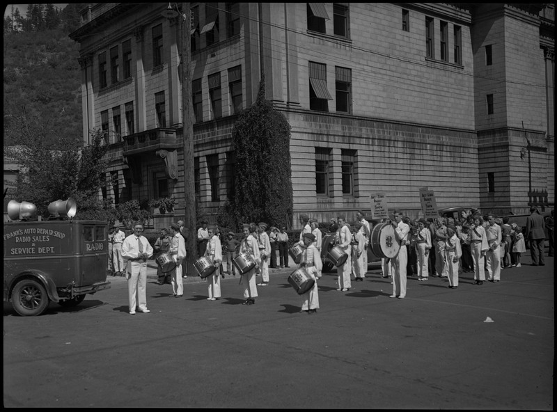 A marching band waiting for the back-to-school parade. A man, possibly the conductor, stands in front of the children in the marching band.