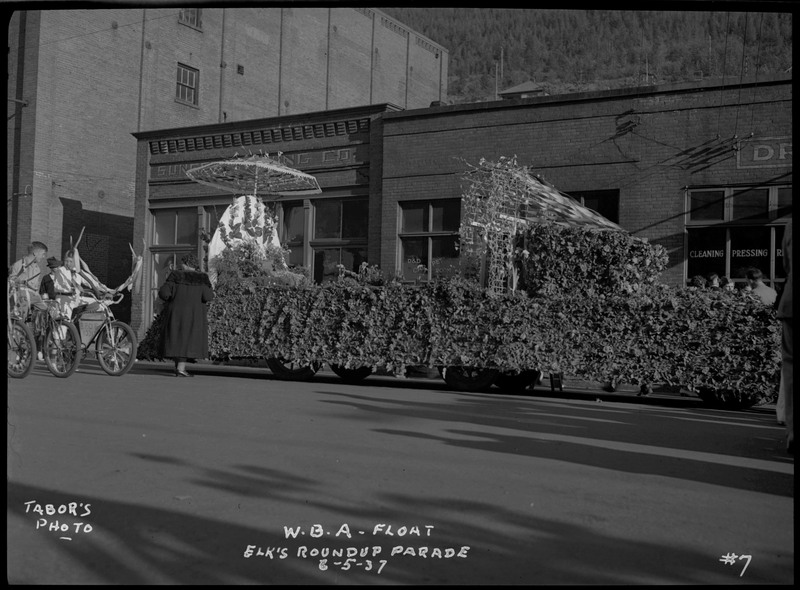 The W.B.A. float decorated with foliage in the Benevolent and Protective Order of Elks parade. Two boys on bicycles can be seen on the left.
