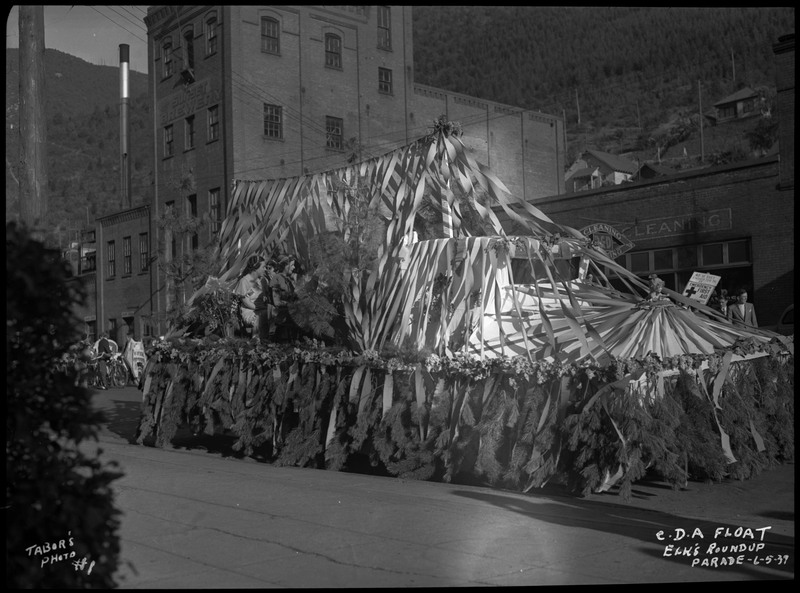 Decorated C.D.A. float during the Benevolent and Protective Order of Elks roundup parade. Three women can be seen sitting on the float, which is highly decorated with streamers and foliage. 