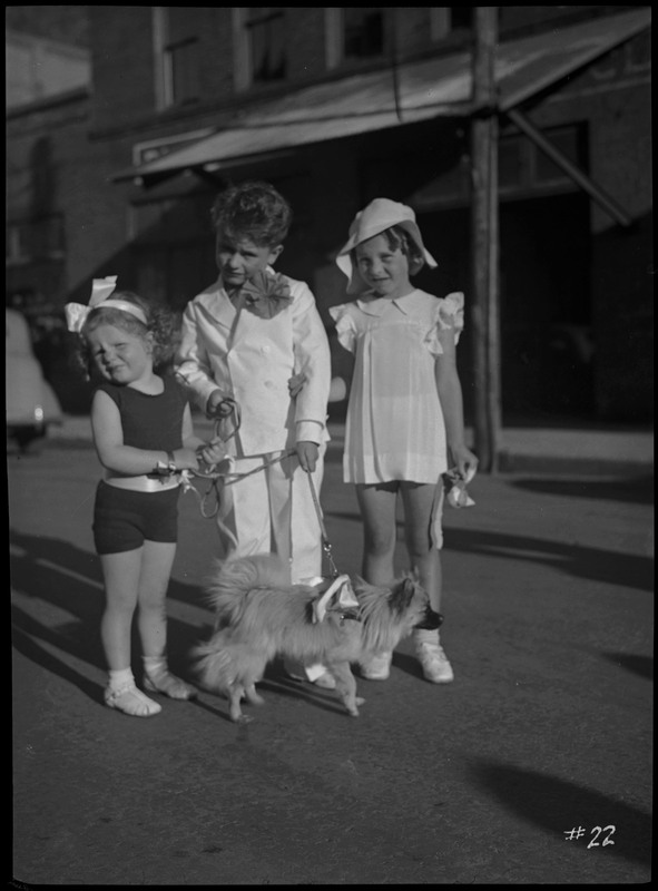 Three young children holding a pet dog during the Benevolent and Protective Order of Elks roundup parade.