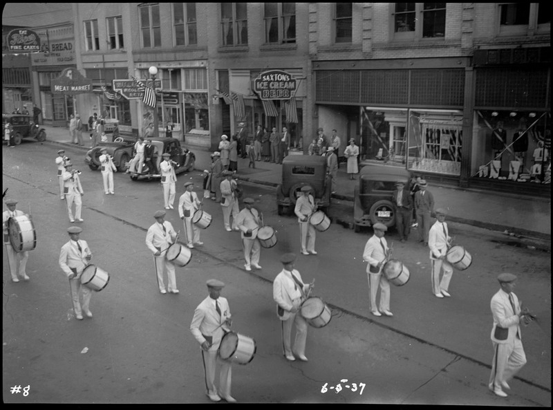 Marching band performing during the Benevolent and Protective Order of Elks roundup parade. Spectators watch from the sidewalk and near parked cars.