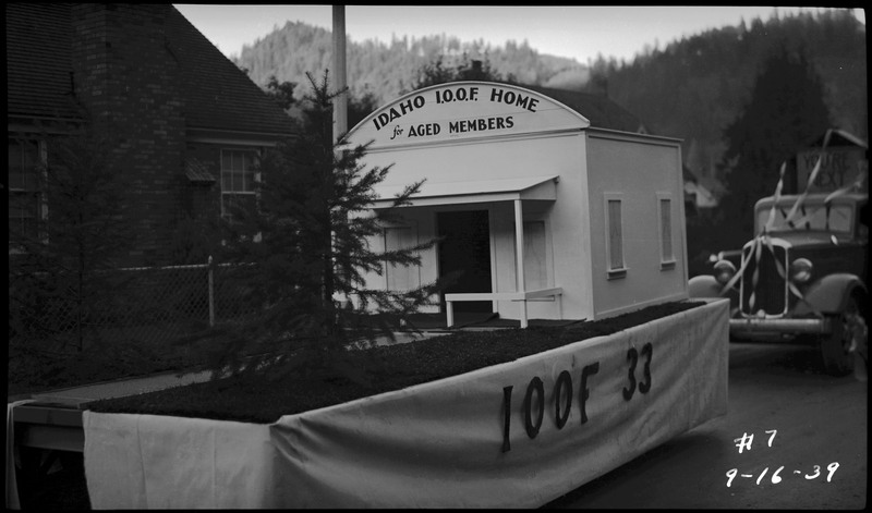 Float decorated with a small tree and a replica of a building with the text, "Idaho I.O.O.F. Home for Aged Members" on the top of the replica building during the Benevolent and Protective Order of Elks roundup parade.