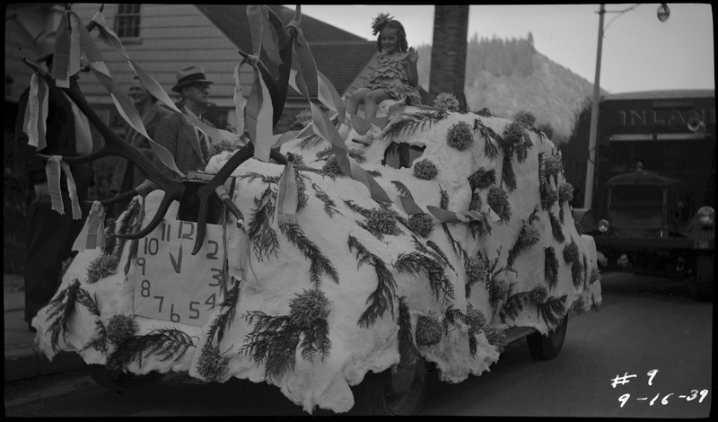 A girl sitting on the top of a automobile decorated as a float with tree branches and fake antlers during the Benevolent and Protective Order of Elks roundup parade.