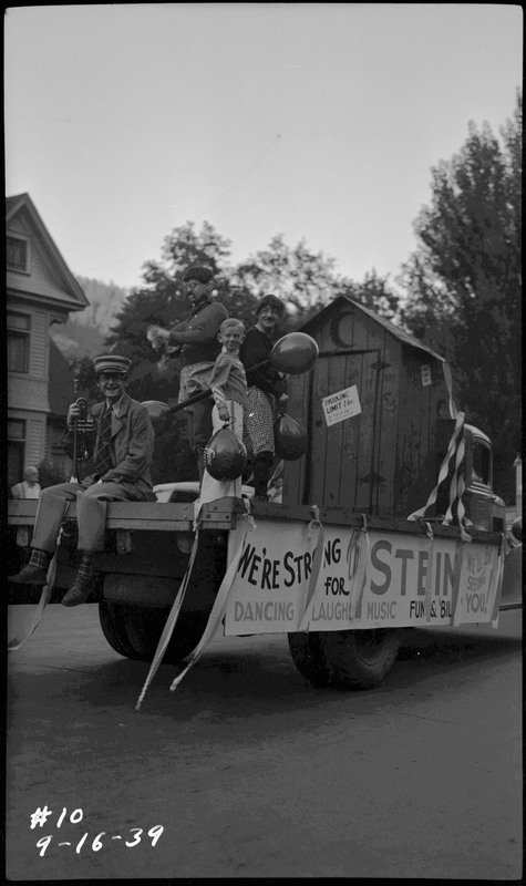 Four people dressed up in costume on a float during the Benevolent and Protective Order of Elks roundup parade. The side of the float reads, "We're Strong for [illegible] Stein," "Dancing, Laughing Music Fun & Bil[illegible]," and "We'll be seeing you!"