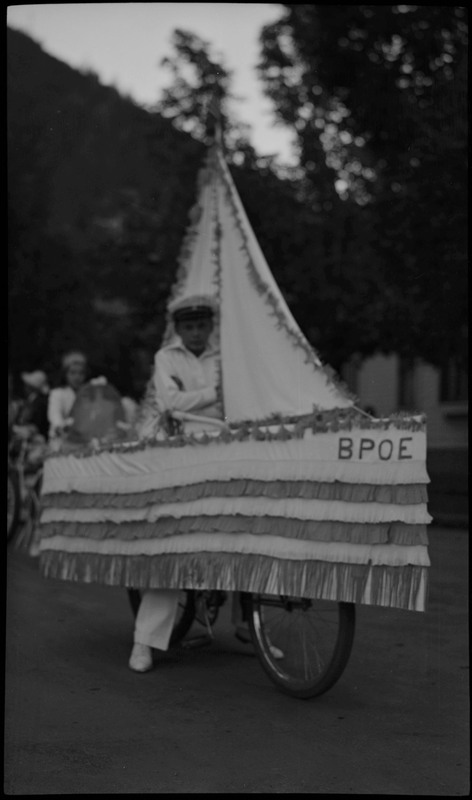 A boy dressed up as a sailor sitting on a bike decorated to look similar to a boat and the words "BPOE" decorated on the edge during the Benevolent and Protective Order of Elks day parade.