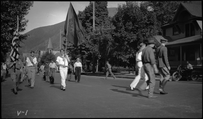 People walking in the street during the V.F.W. State convention parade. Two people are holding flags.