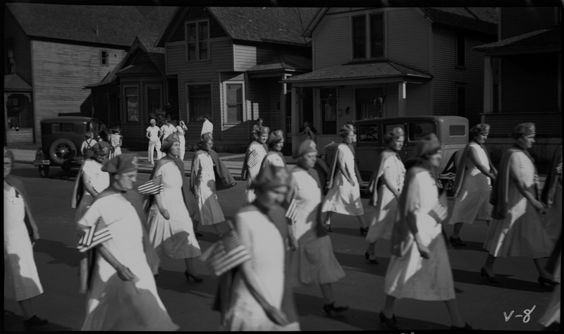 Women in matching uniforms and holding small American flags walk in the V.F.W. State convention parade.
