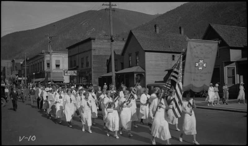 Women wearing white, three holding American flags walking in the V.F.W. State convention parade.