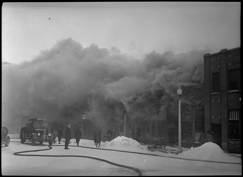 Smoke escapes the McKinley Building while the fire continues. Several people can be seen near the building, either passing by or watching. A firetruck is standing by.