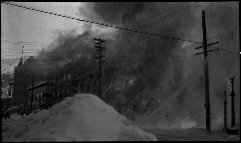 Smoke billows out of the Ryan Hotel and Tabor building fire as firefighters attempt to put the fire out. A large mound of snow is in the foreground.