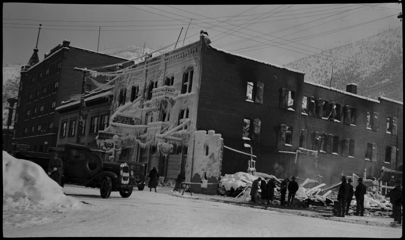 View of the Ryan Hotel and Tabor Building after a fire. Soot and what appear to be icicles and frost cling to the structure of a building after a fire. There appear to be no window panes anymore, and there are piles of snow and soot on the ground. There are several people in the standing near the damage.