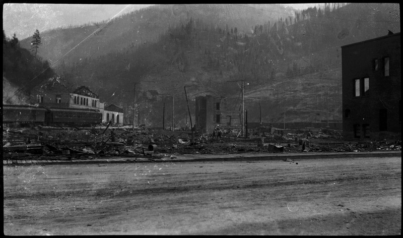 View of ruins across a street in a smoky haze after a fire.