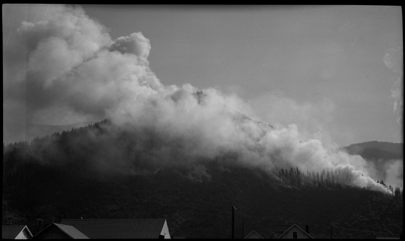 Smoke rises from the montane forest in the distance. Roofs can be seen in the foreground.