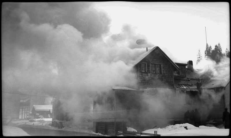 Smoke rising from the Pearson house fire. Three people can be seen putting out the fire on the right and another person is watching the fire.
