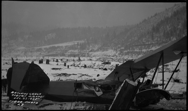 Remnants from an airliner crash. Snow covered trees and mountains in the background. Caption on the bottom left of the photograph reads "Airplane Crash Osburn Airport Dec. 27, 1933 Tabor Photo A3."