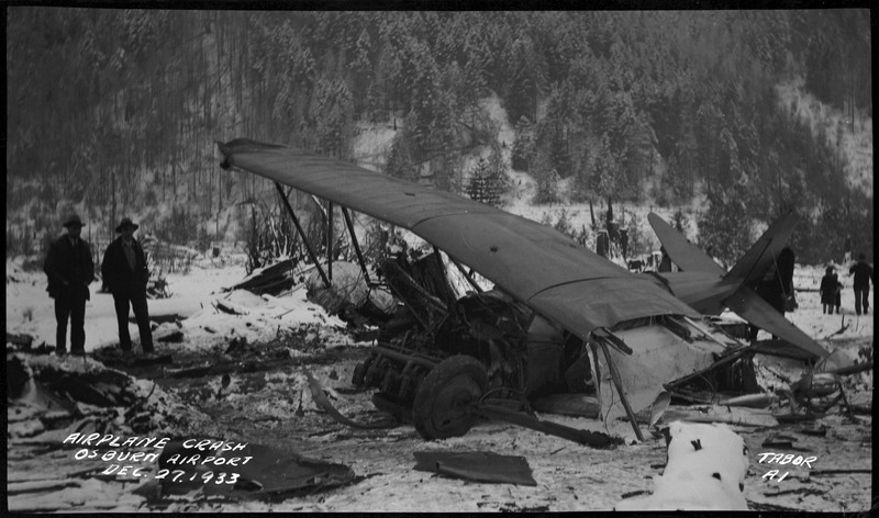Two men look at the remnants of an airliner crash in the snow. Caption on the bottom left reads "Airplane crash Osburn Airport Dec. 27, 1933."